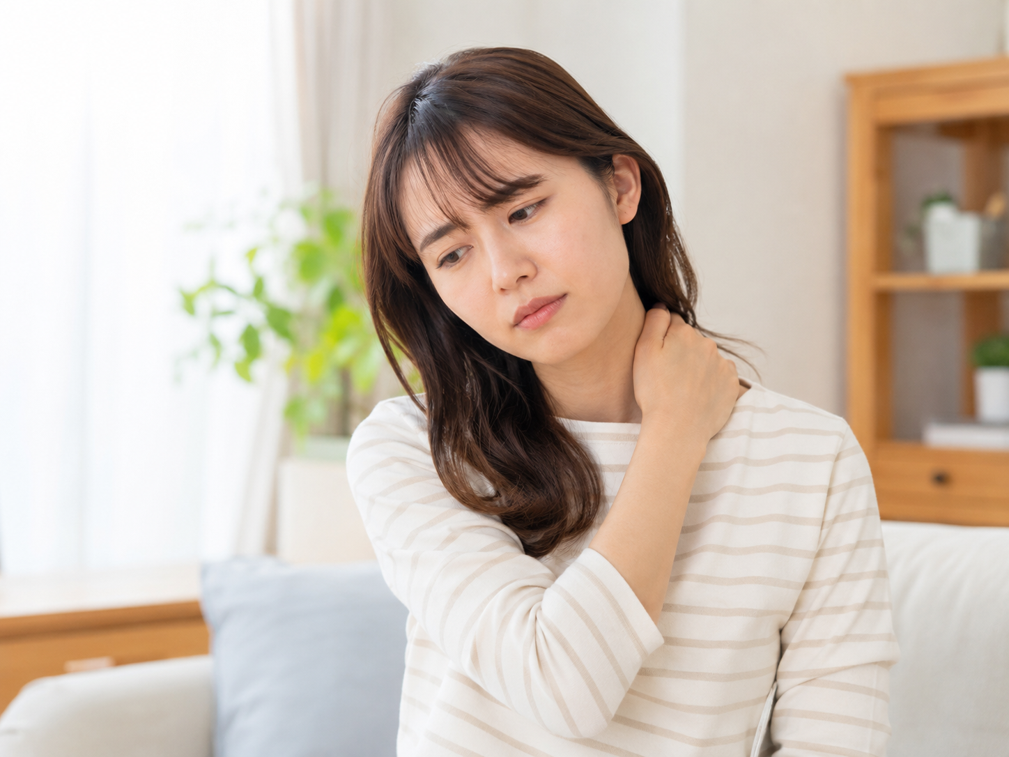 夏前の室内で体のだるさや肩こりを感じている女性