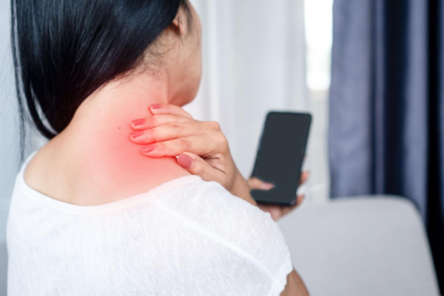 スマートフォンを見ながら首や肩がつらそうな女性のイメージ