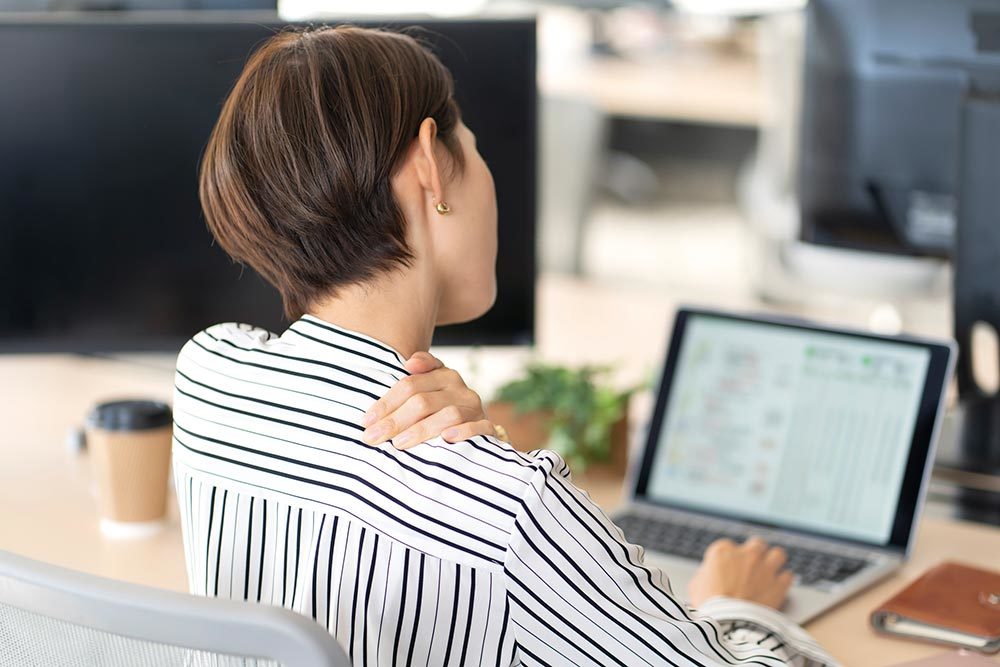 長時間のデスクワークで肩が凝ってつらい女性の写真です。