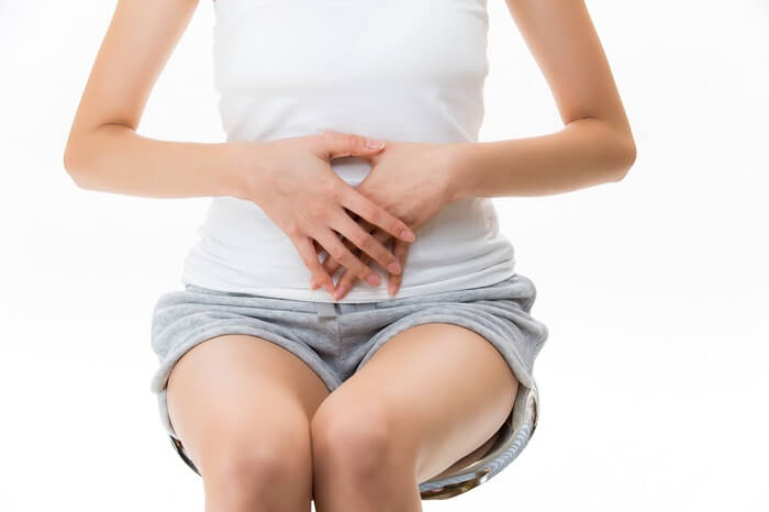 椅子に座り両手をお腹に当てて腹式呼吸を行っている女性の写真です。