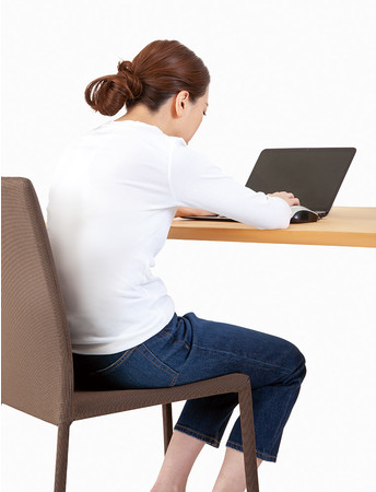 長時間同じ姿勢でデスクワークをしている女性の写真です。