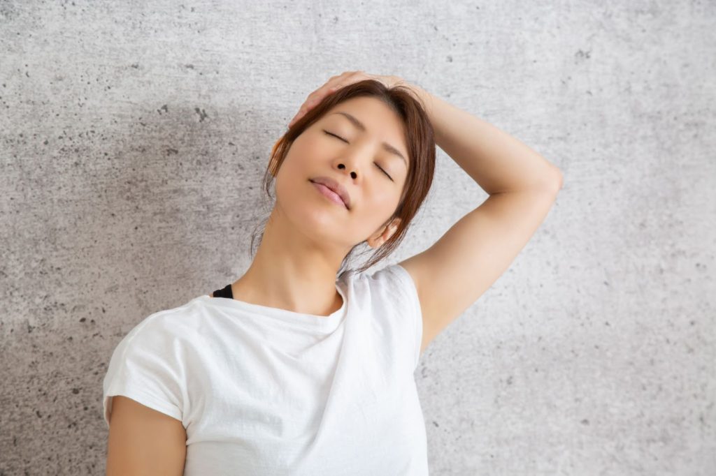 首をゆっくりストレッチしている女性の写真です。